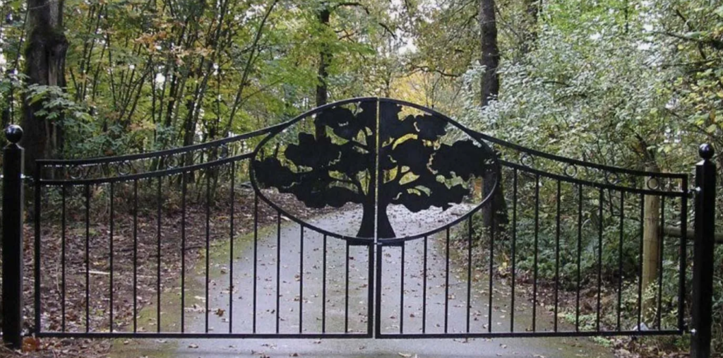 2 panel custom wrought iron driveway entry gate with an iron fabricated tree in the center where the two gates meet, protecting the entrance to a tree lined driveway in East Texas
