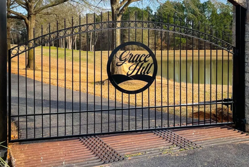 Custom wrought iron gate for driveway entry with the words Grace Hill fabricated into the center of the gate installed at the beginning of a long driveway