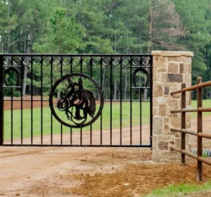 black custom wrought iron driveway entry gate with horse head emblem in the center, attached to stone column entrance to a Texas driveway